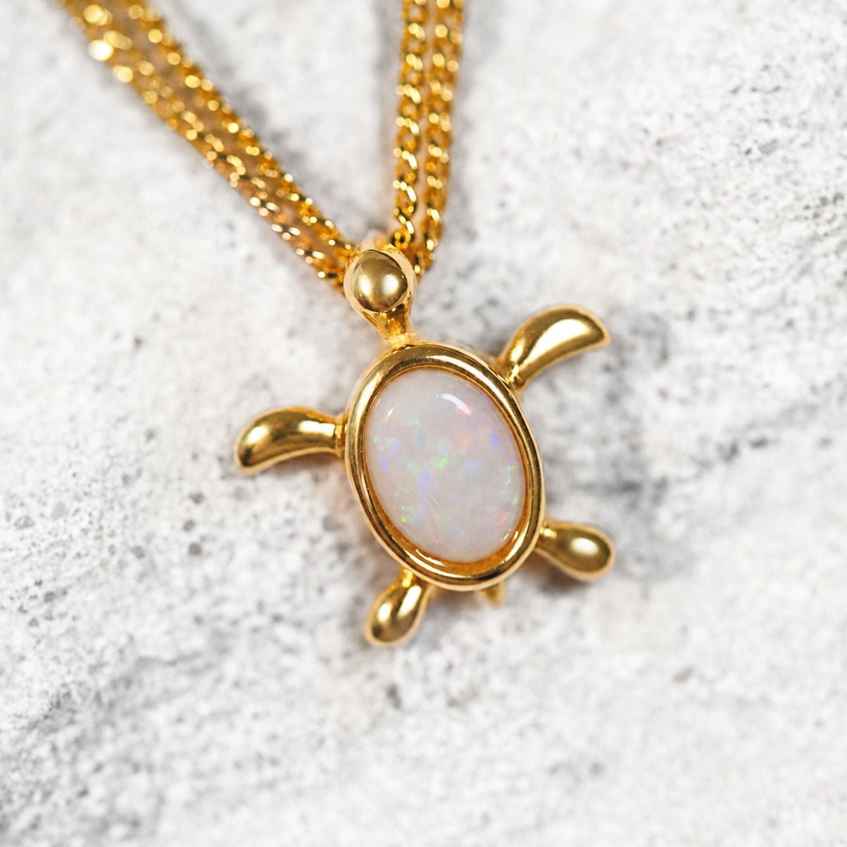 Gold turtle pendant with a white opal stone on a textured gray background