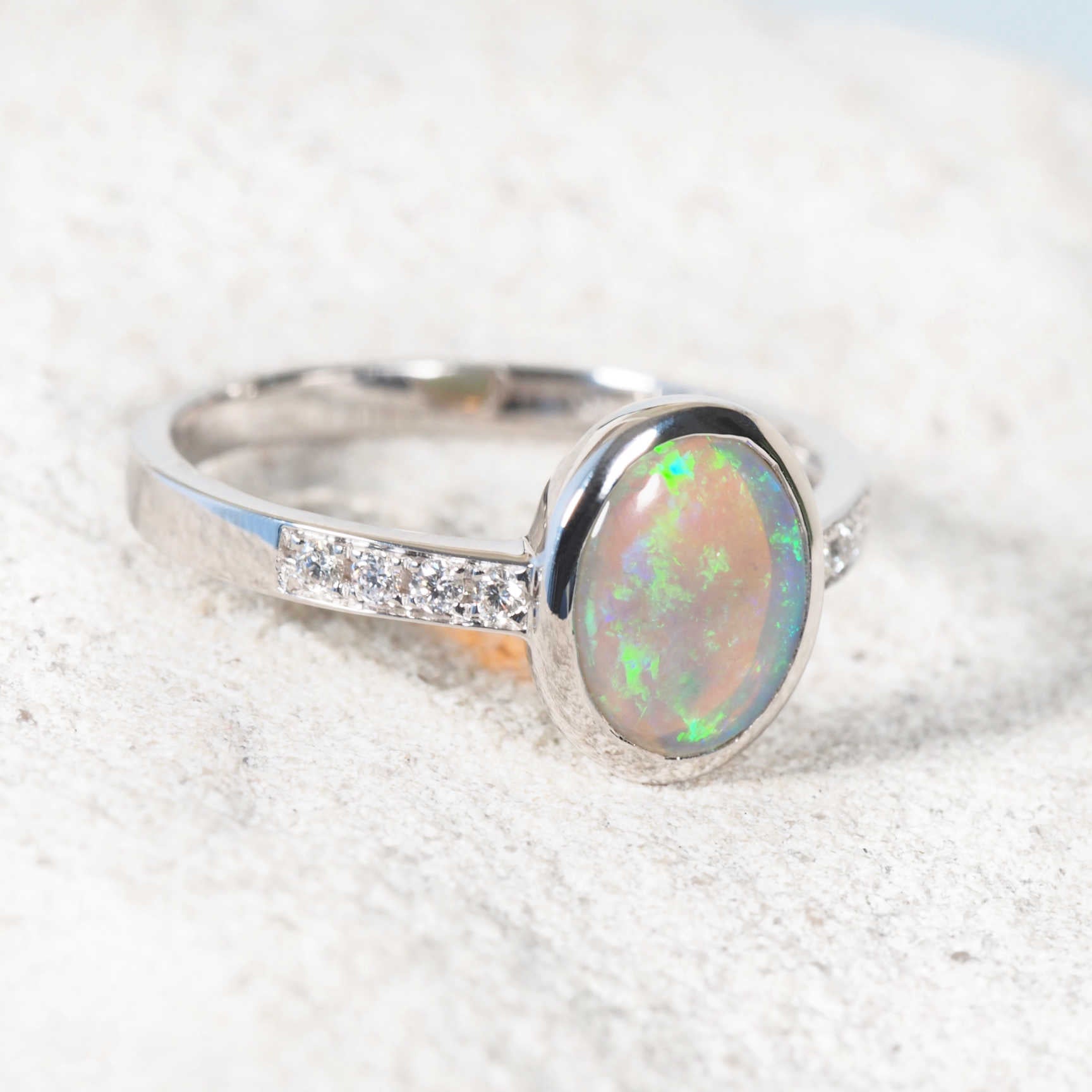 Close-up of Lightning Ridge green opal ring with bezel-set diamonds on each shoulder