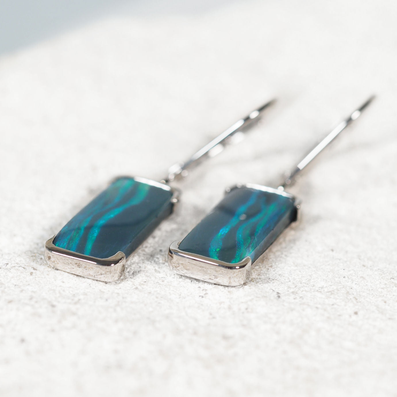 Close-up of 'Corinna' opal earrings showing bezel-set solid black opals glowing green in polished white gold