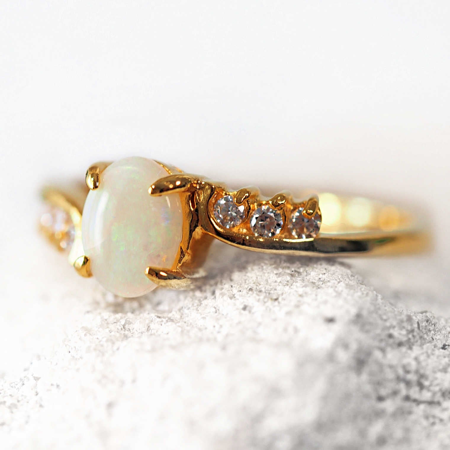 Gold ring with a large opal stone and smaller diamonds on a textured white surface