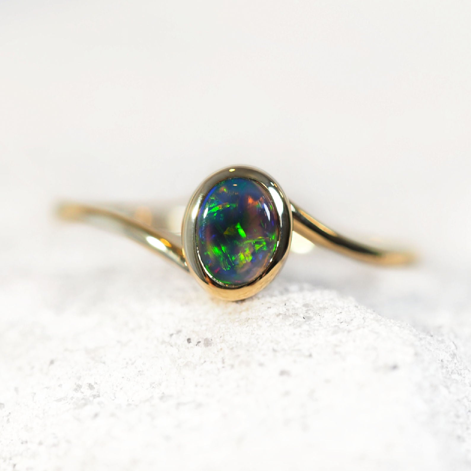 Gold ring with a green black opal stone on a white background
