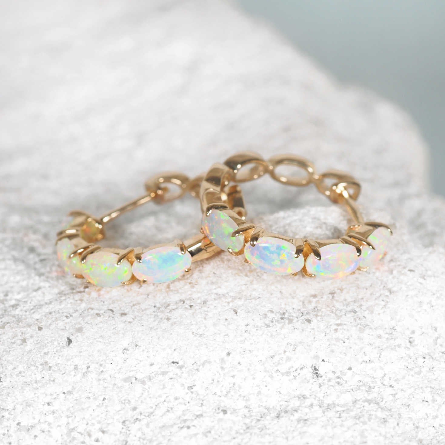 Close-up of claw-set crystal opals in handcrafted gold hoop earrings