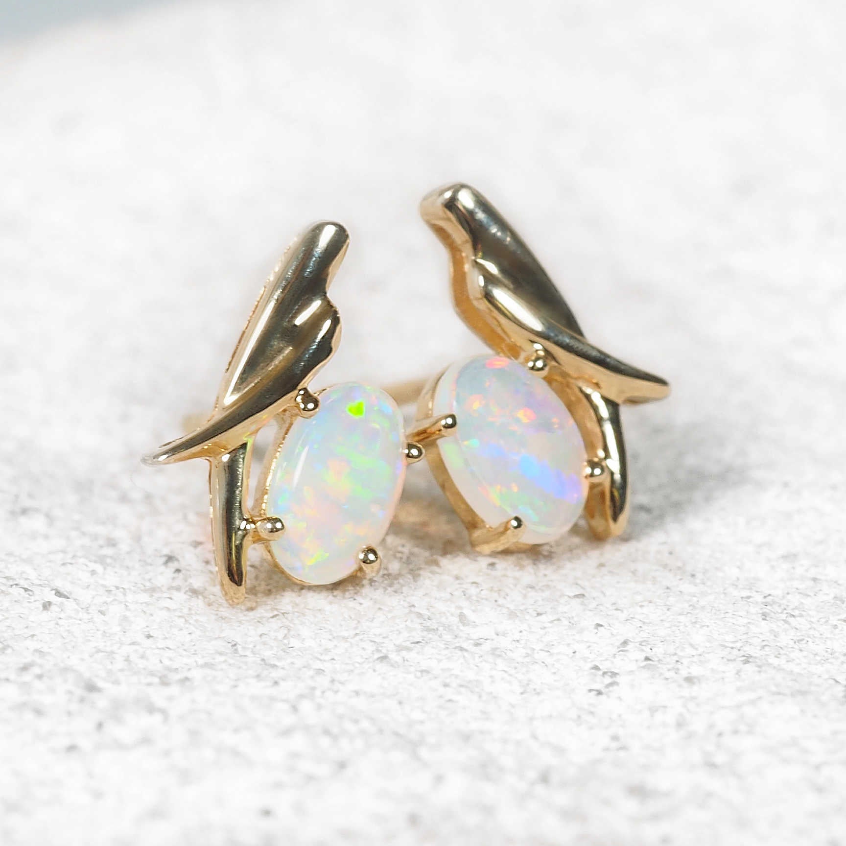 Close-up of vibrant multi-coloured crystal opals claw-set in 'Lunessa' gold earrings