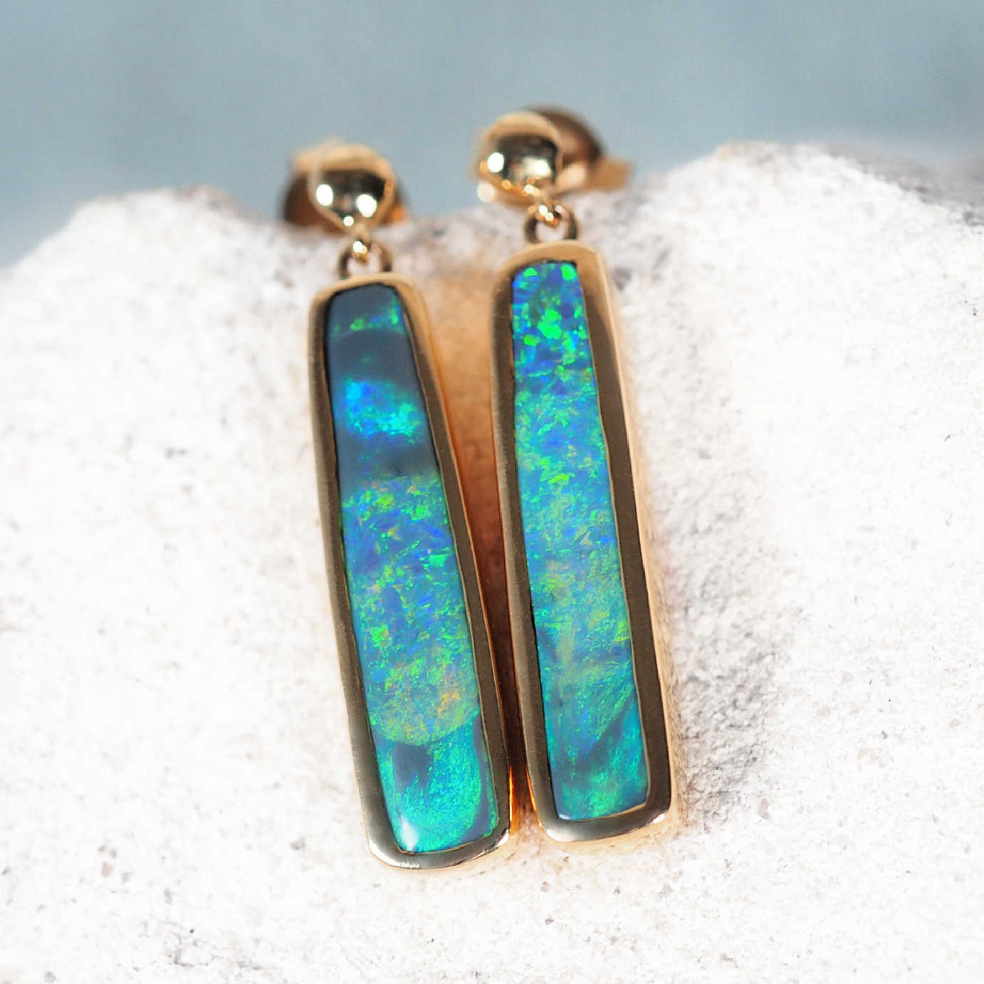 'Margareta' black opal stud earrings in 14ct yellow gold with rectangular Lightning Ridge opals showing vivid green and blue flashes.