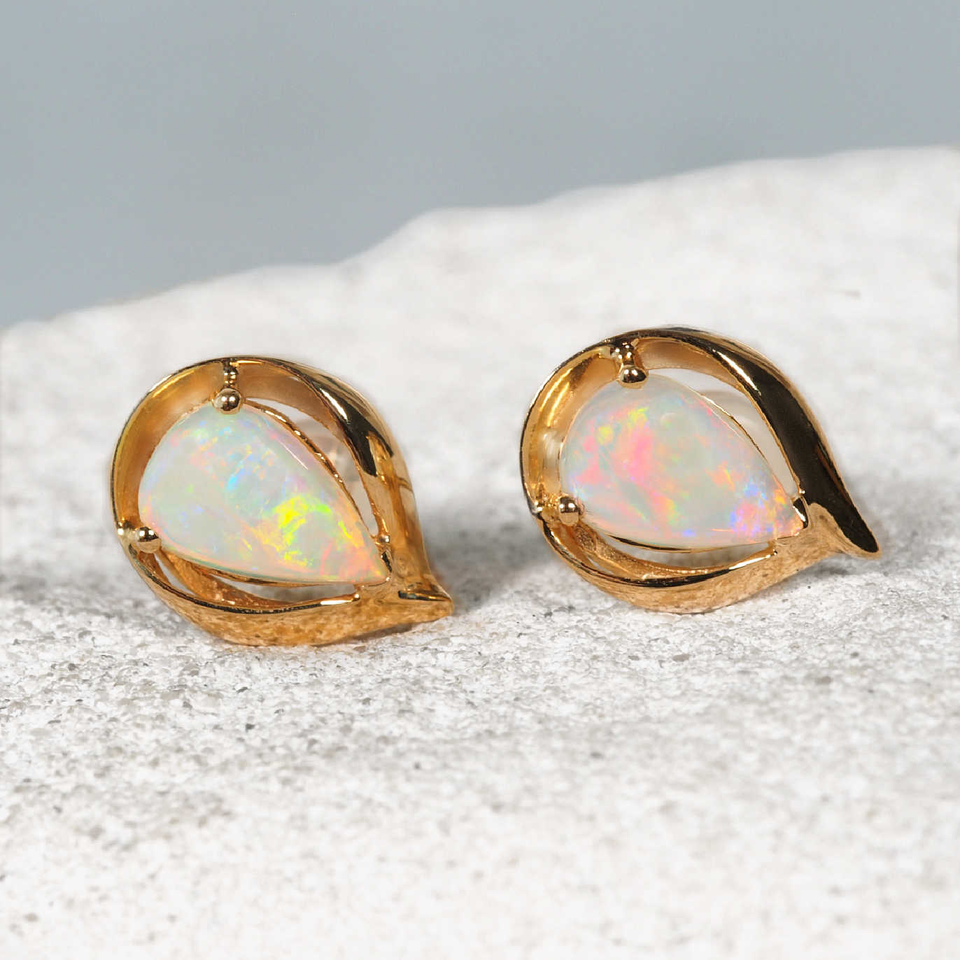 Pair of gold earrings with colourful opal stones on a textured surface