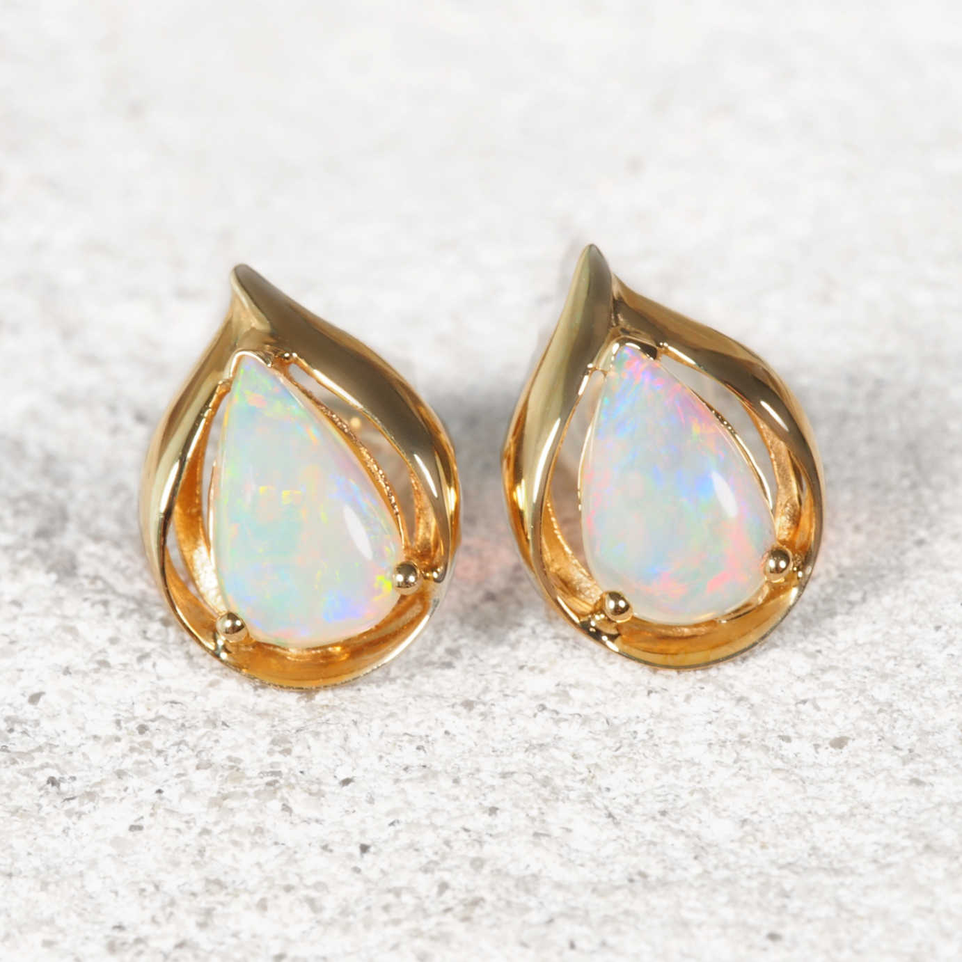 Pair of gold opal earrings with Australian opal stones on a textured white background