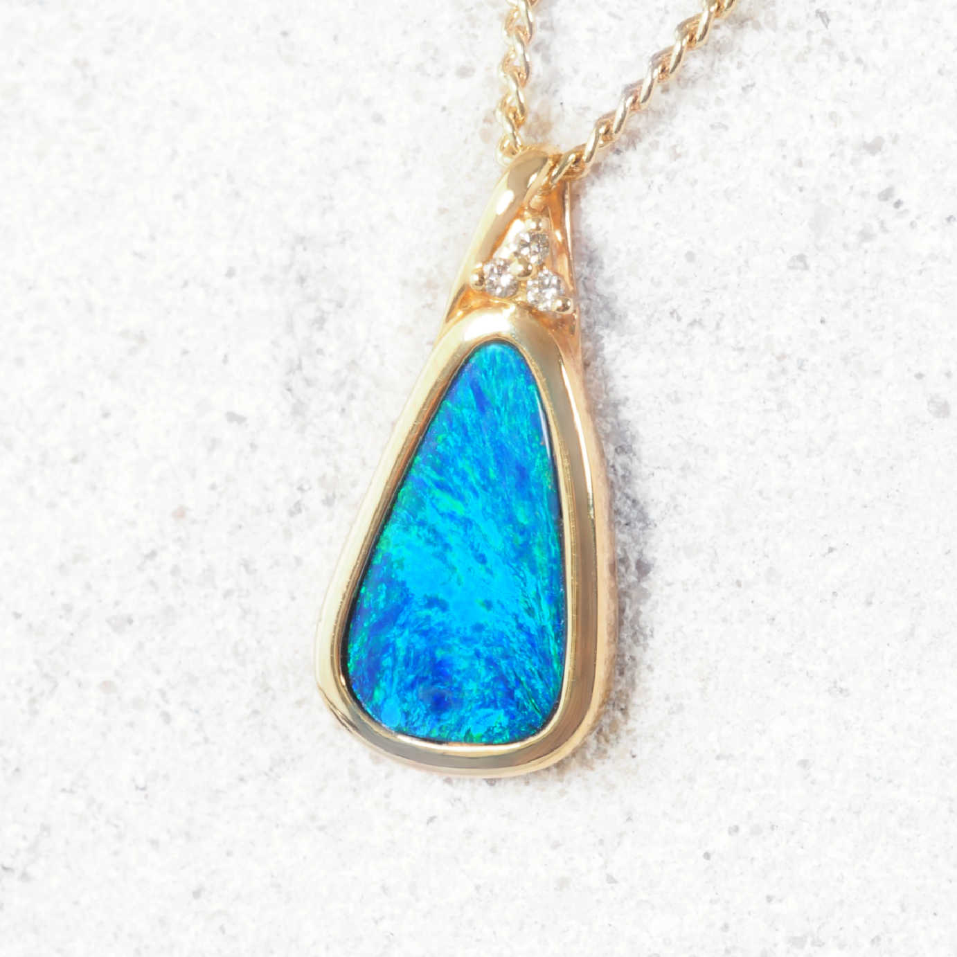 Elegant gold pendant with bezel-set Australian opal and trio of white diamonds.