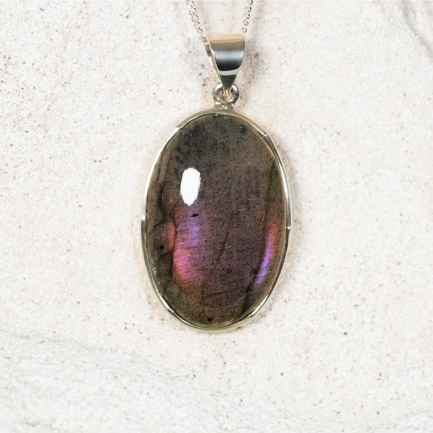 Labradorite pendant on a silver chain against a textured white background