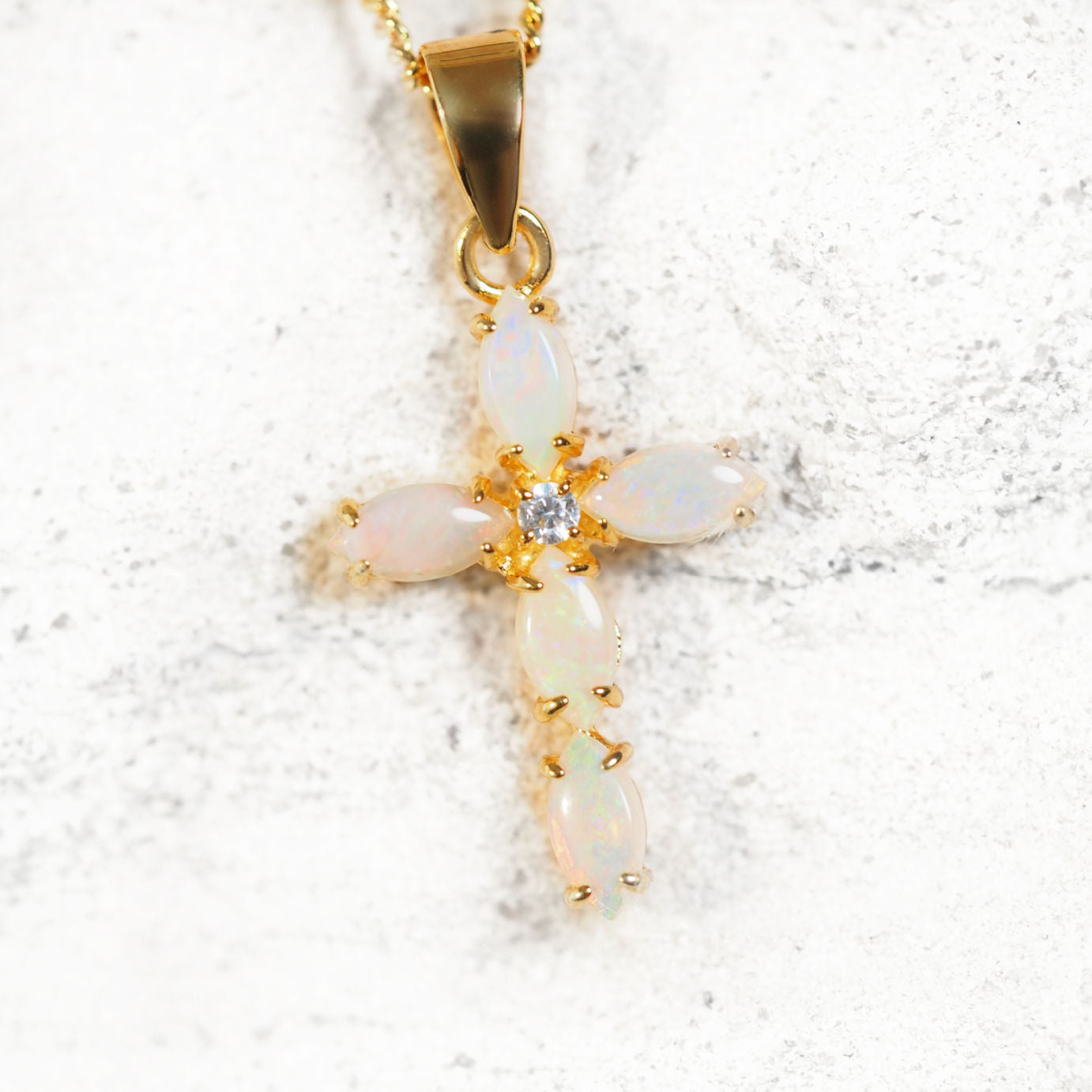 Gold cross pendant with opal stones on a white background