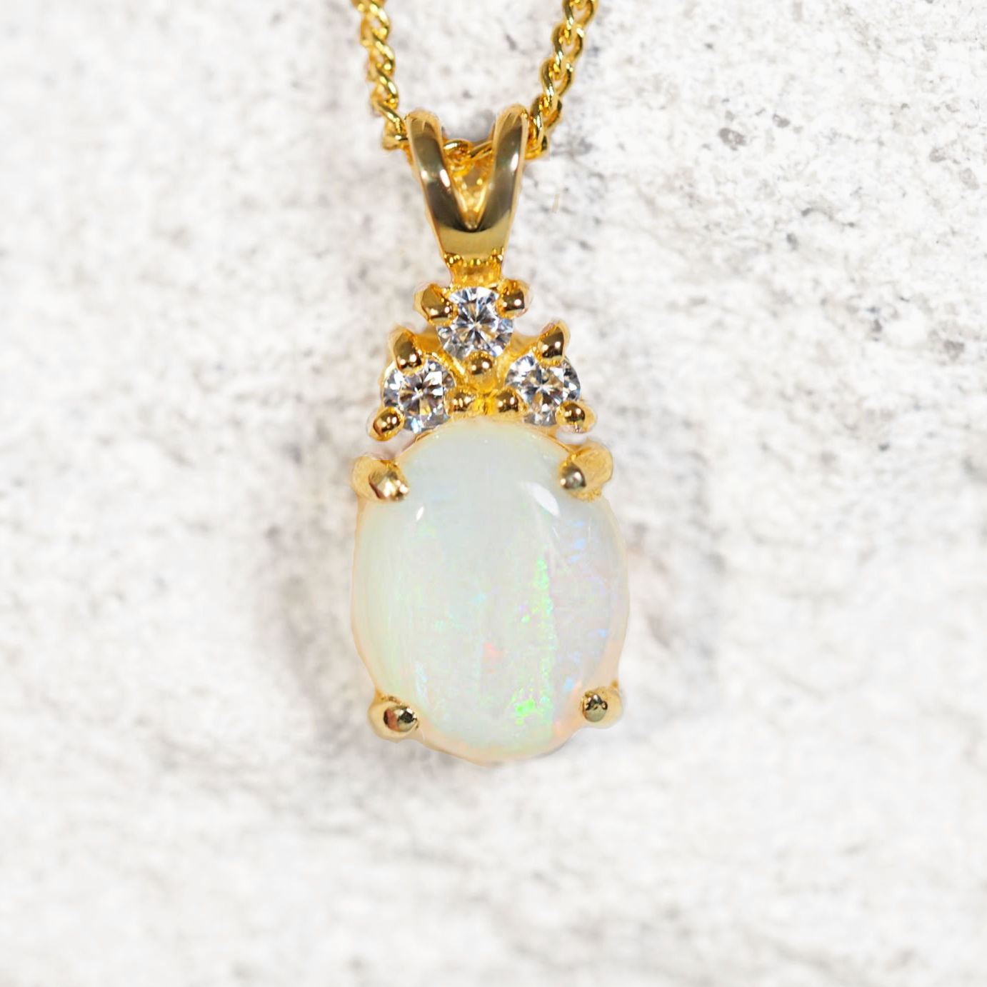 Gold pendant with a green opal gemstone on a textured white background