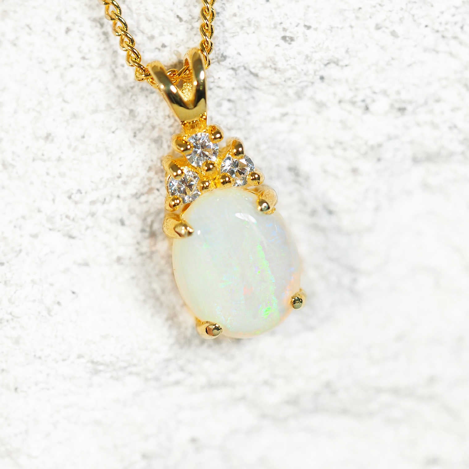 Gold pendant with a white opal gemstone on a textured white background