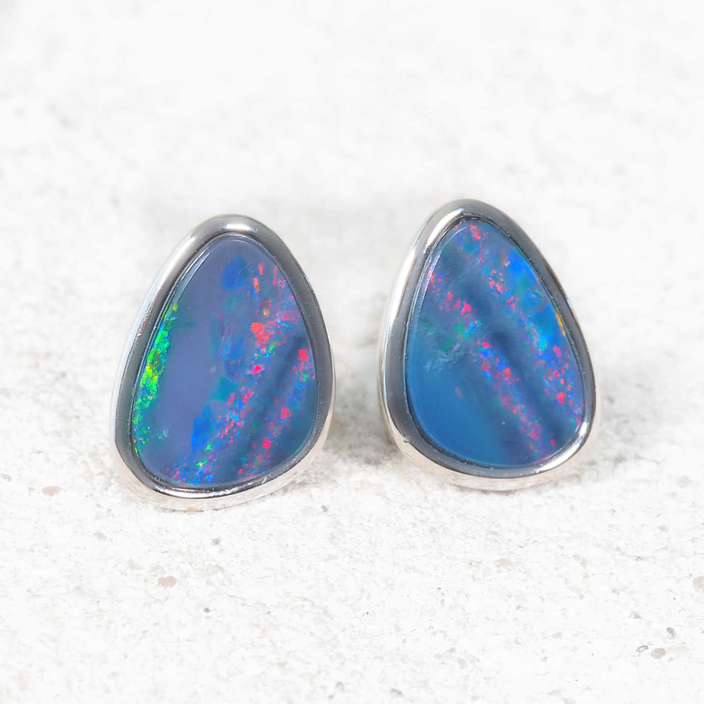 Teardrop-shaped opal earrings with colorful interior on a textured white background