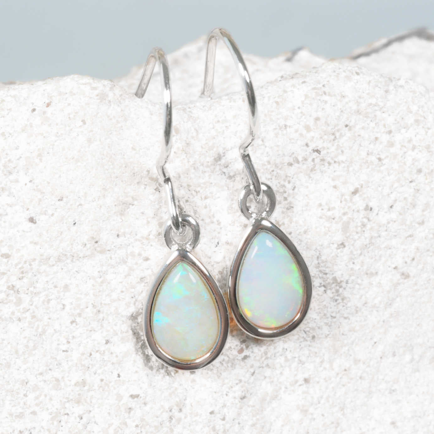 Blue and green opal earrings on a textured white surface