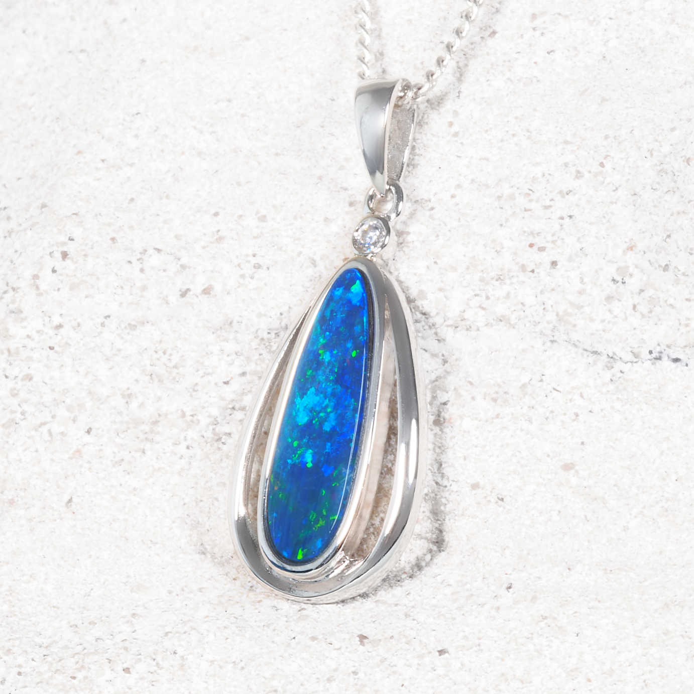 Teardrop-shaped blue opal pendant with silver setting on a white background