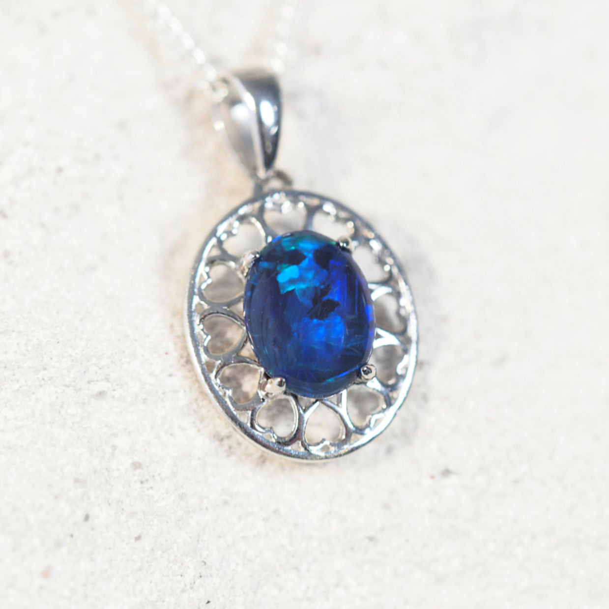 'Amore Blue' opal pendant in sterling silver with heart-pattern design and claw-set oval Australian triplet opal in vivid blue and green tones