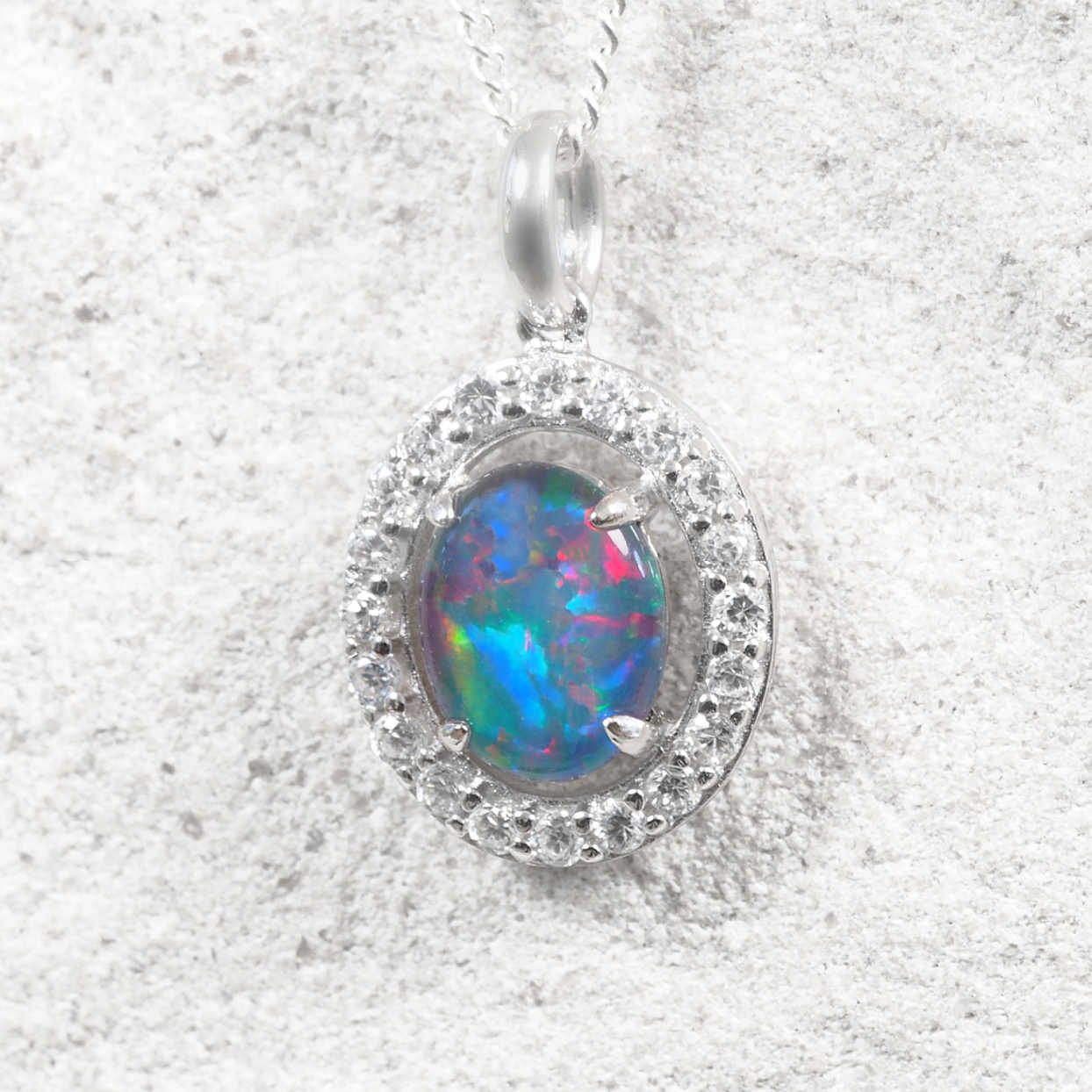Australian triplet opal necklace in polished sterling silver with an oval claw-set opal displaying vivid multi-coloured play-of-colour and a cubic zirconia halo.