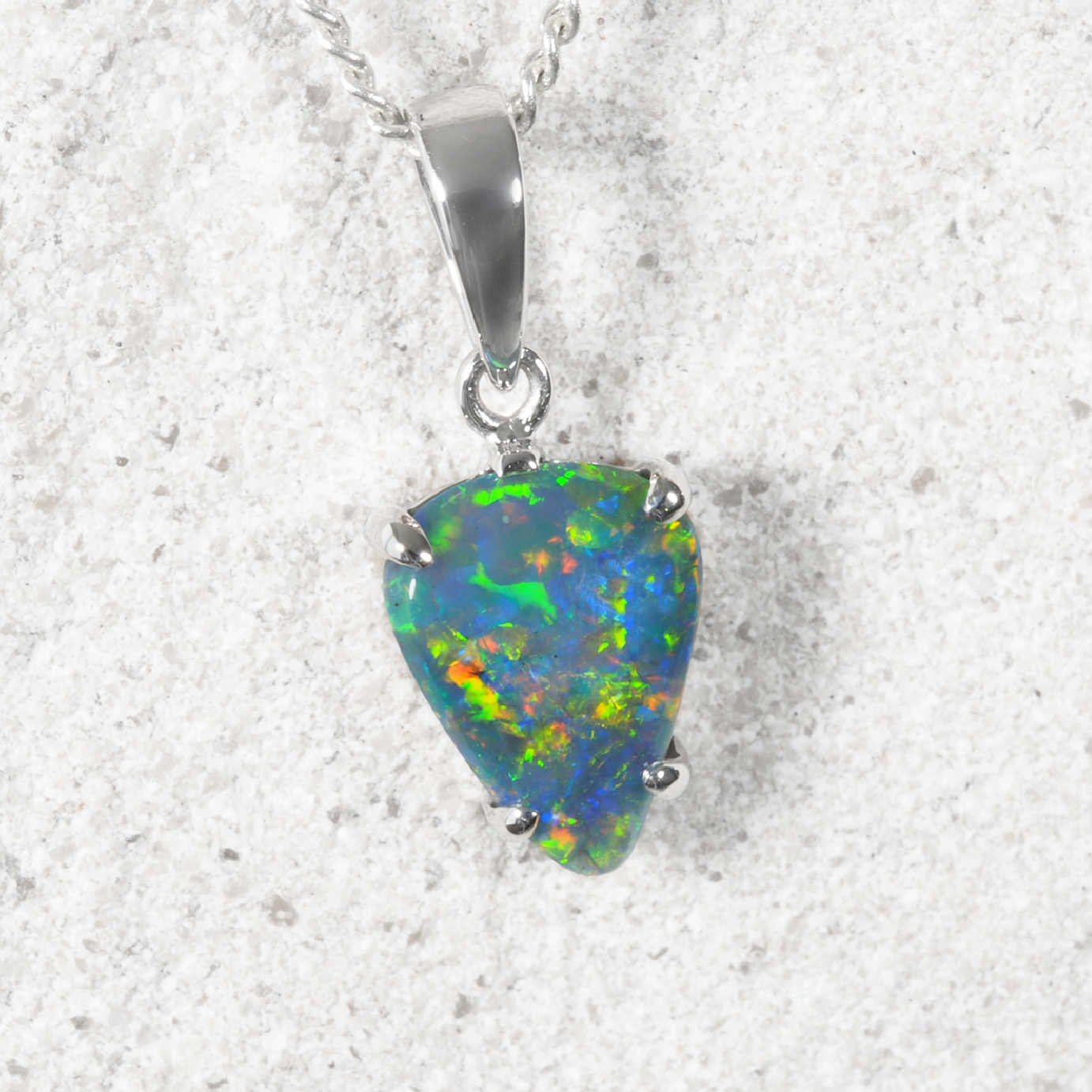 A white gold natural Australian opal pendant necklace featuring a teardrop-shaped opal gemstone with vibrant green, blue, and orange flashes, set in a polished silver bail and prongs against a light gray textured background.