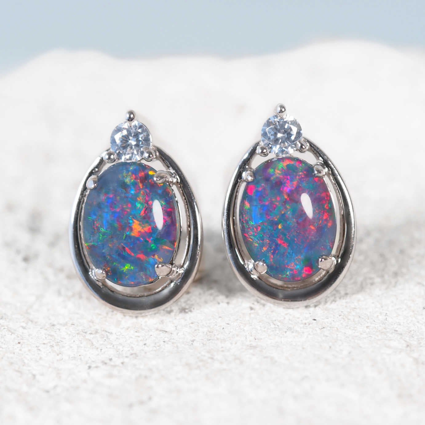 Pair of opal earrings with silver setting on a textured surface