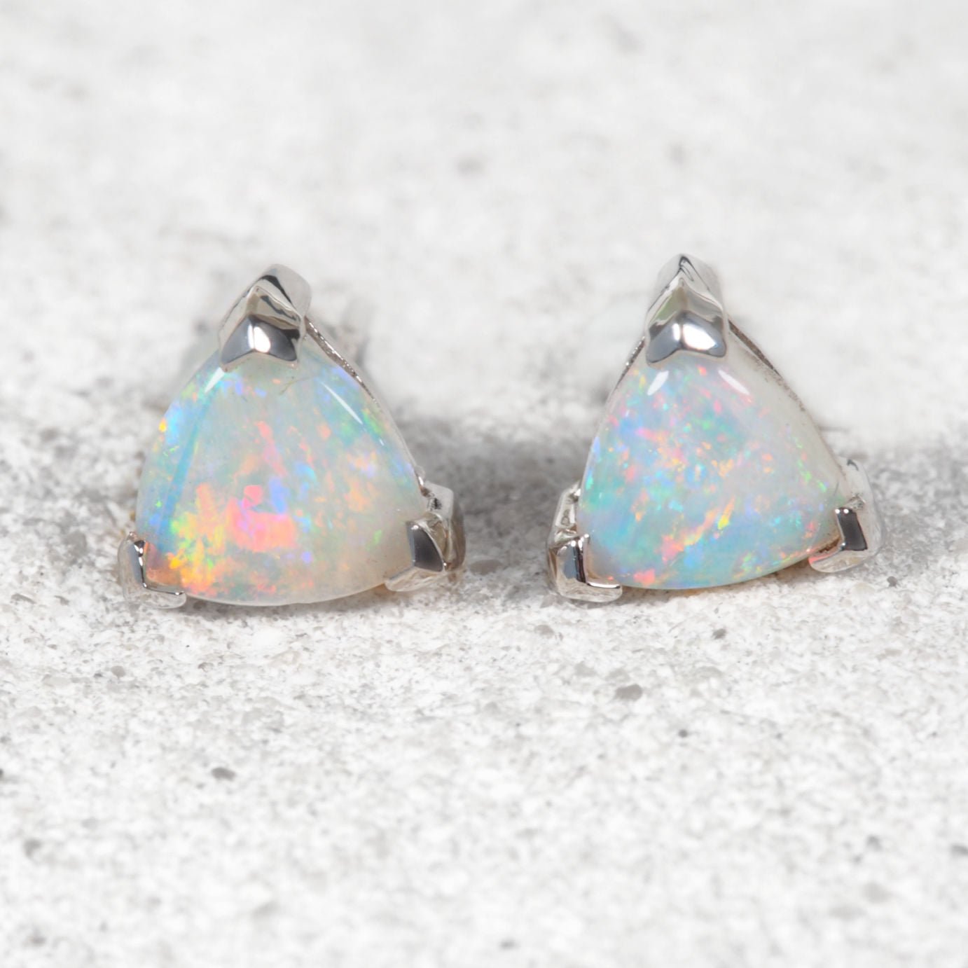 Triangular opal earrings on a textured white background