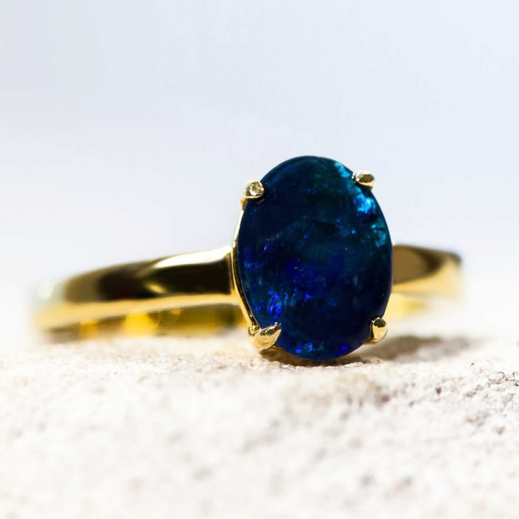 Gold ring with a blue opal gemstone on a white background
