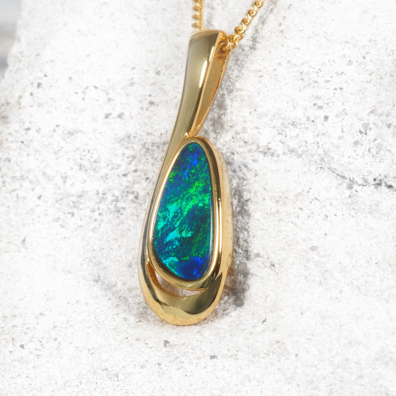 Gold opal pendant with a green gemstone on a textured white background