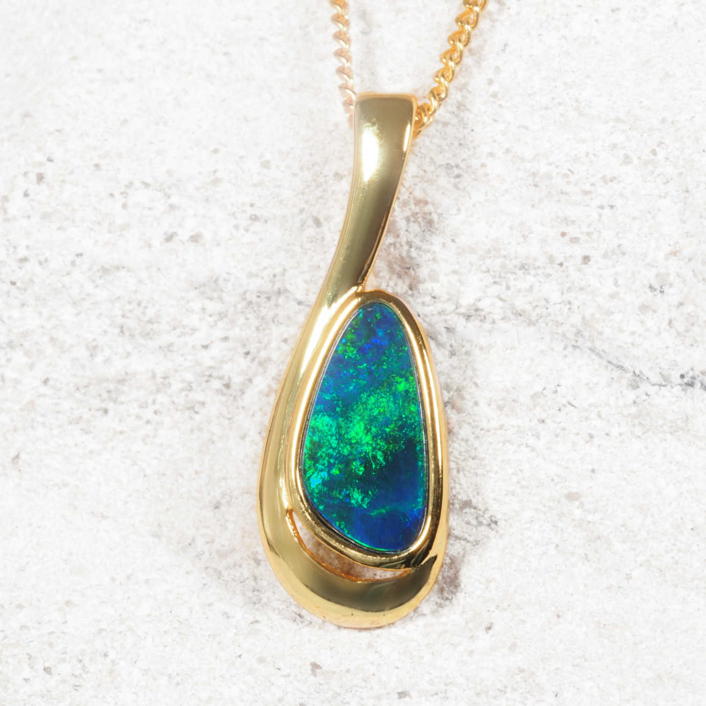 Gold opal pendant with a blue-green gemstone on a textured white background