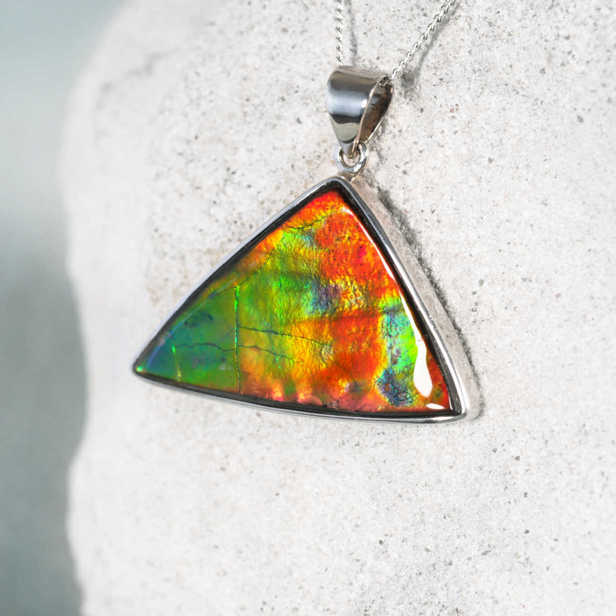 Close-up of 'Althea' pendant featuring a unique Ammolite gemstone with fiery red, green, and blue hues.
