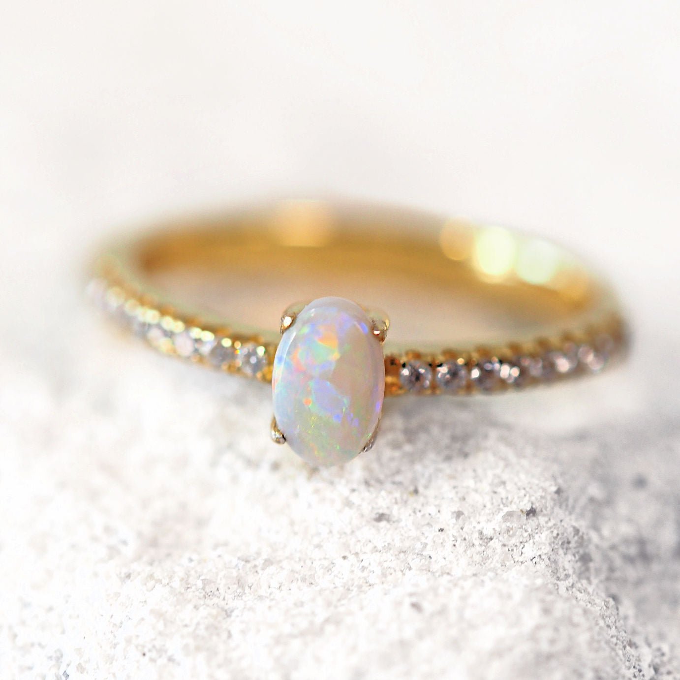 Gold ring with a central opal stone on a textured white surface