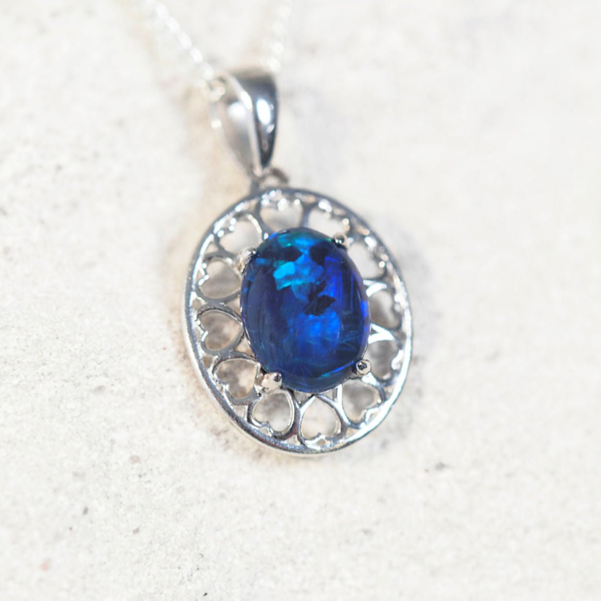 'Amore Blue' opal pendant in sterling silver with heart-pattern design and claw-set oval Australian triplet opal in vivid blue and green tones