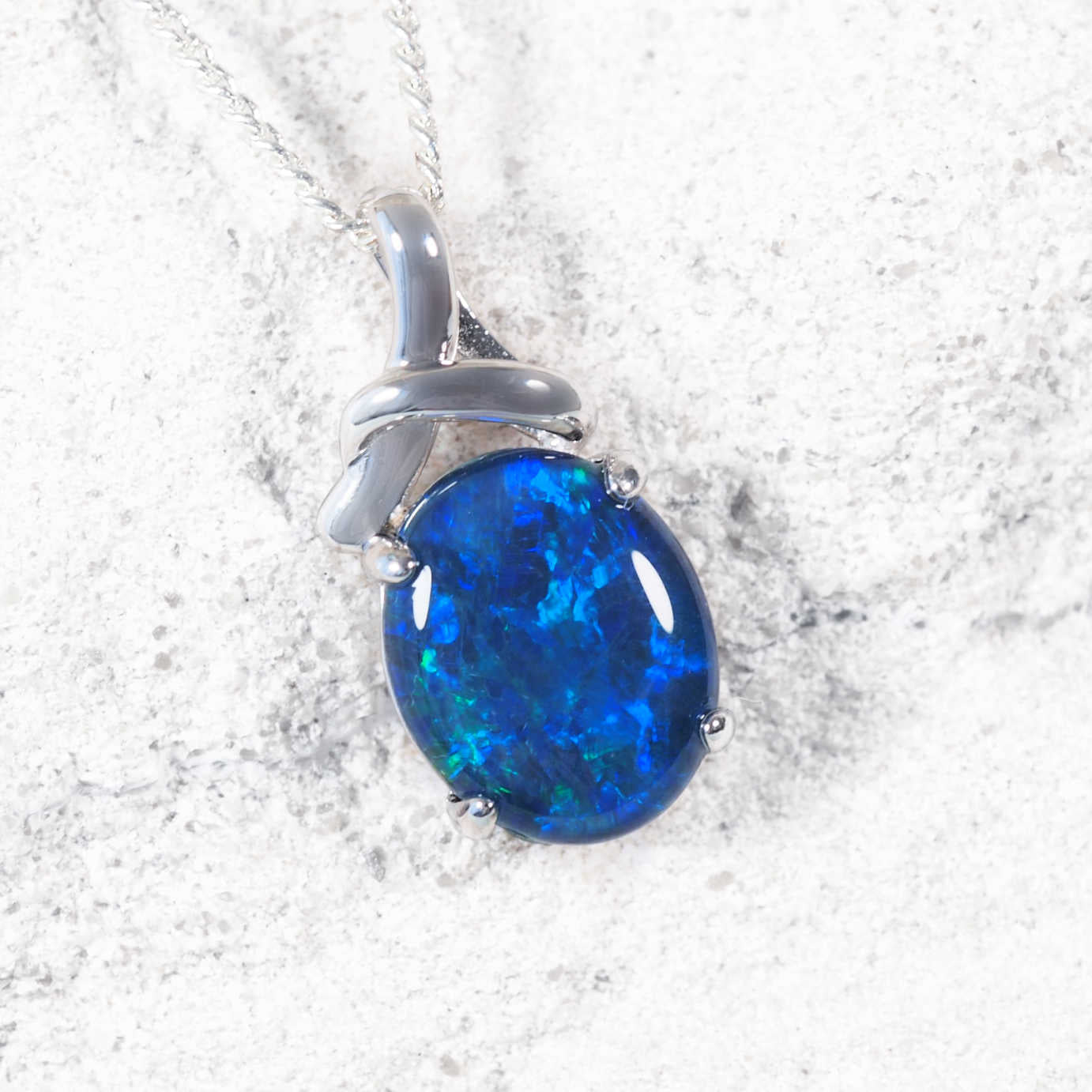 Australian blue opal pendant on a silver chain against a white rock background