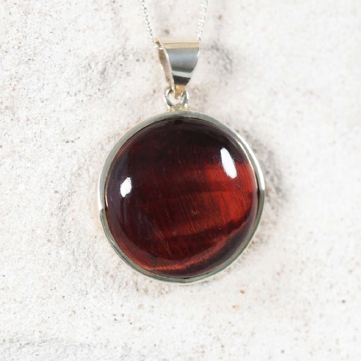 Sterling silver circular pendant featuring genuine Red Tiger’s Eye, glowing with rich brown-red color and natural sheen.