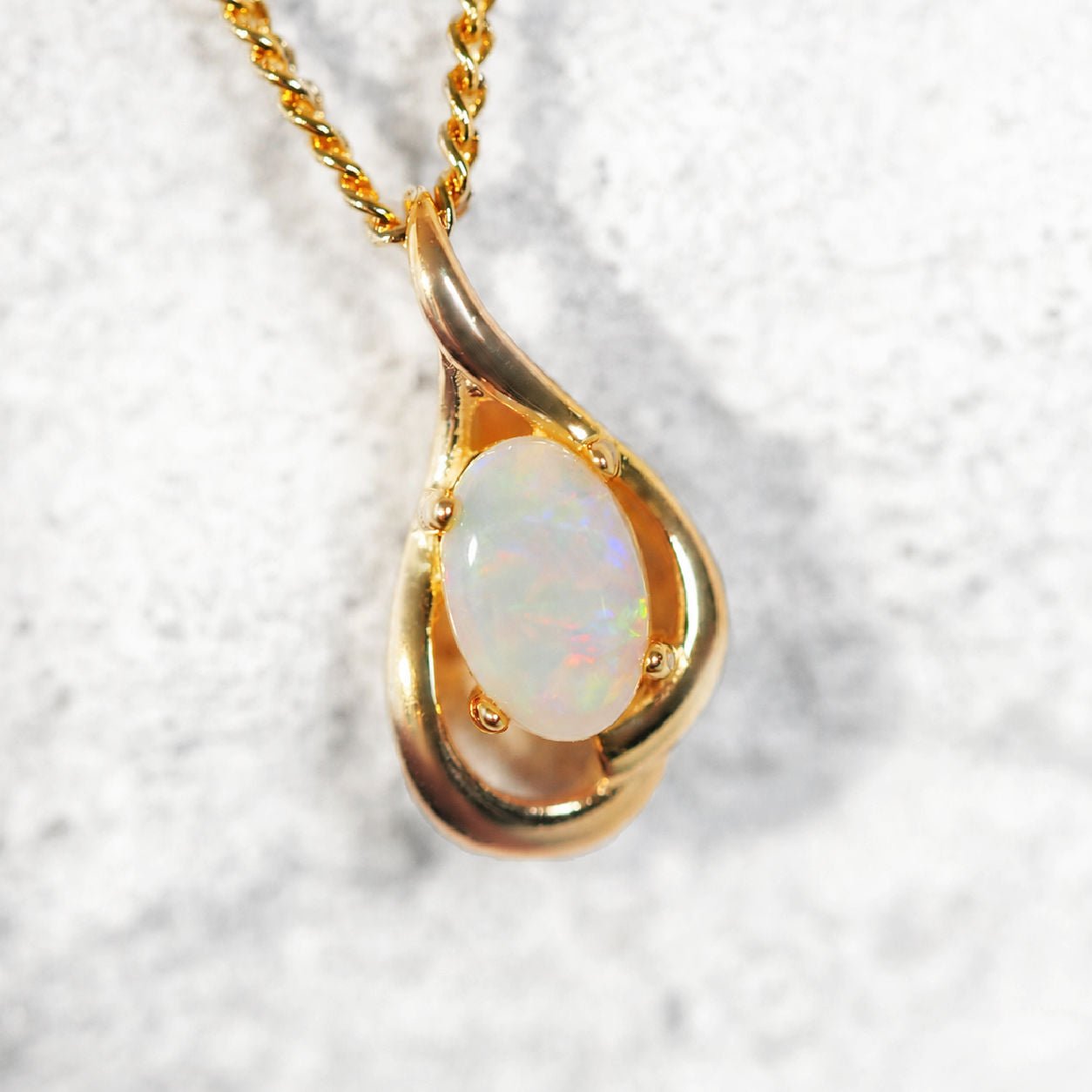 Gold pendant with a white opal gemstone on a textured white background
