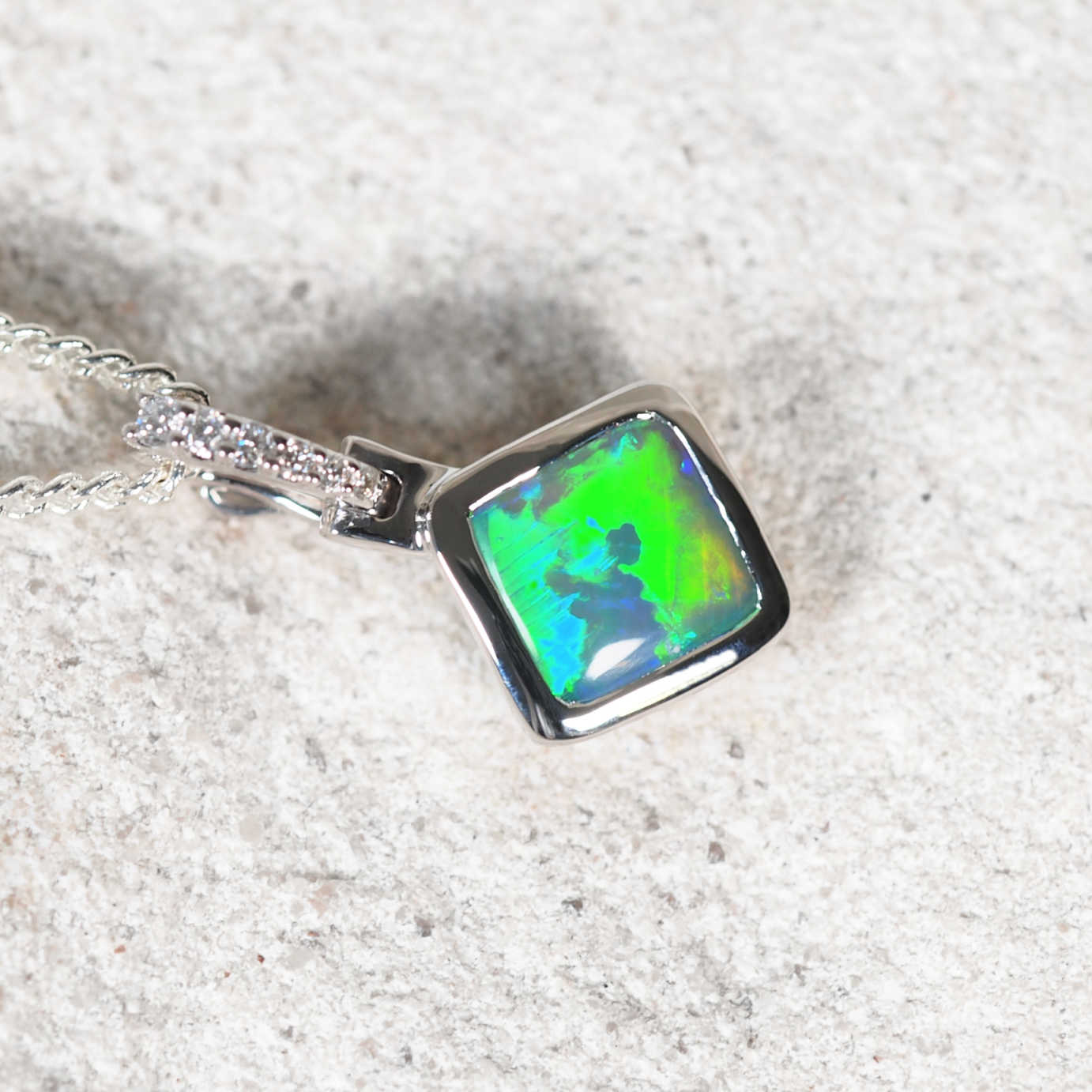 Close-up of square green Lightning Ridge black opal pendant with bezel setting and diamond accents