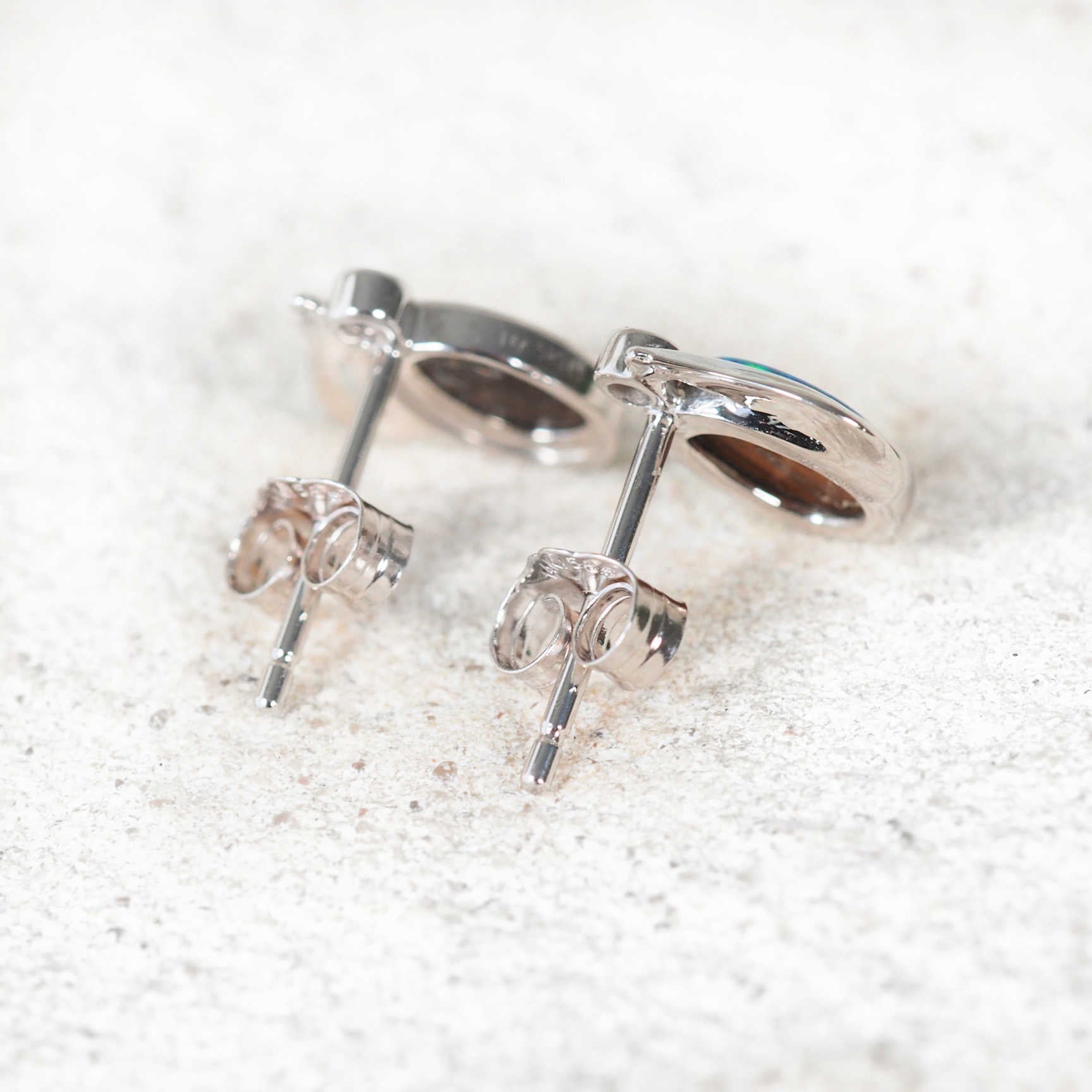 Back of a pair of silver stud opal earrings on a white background