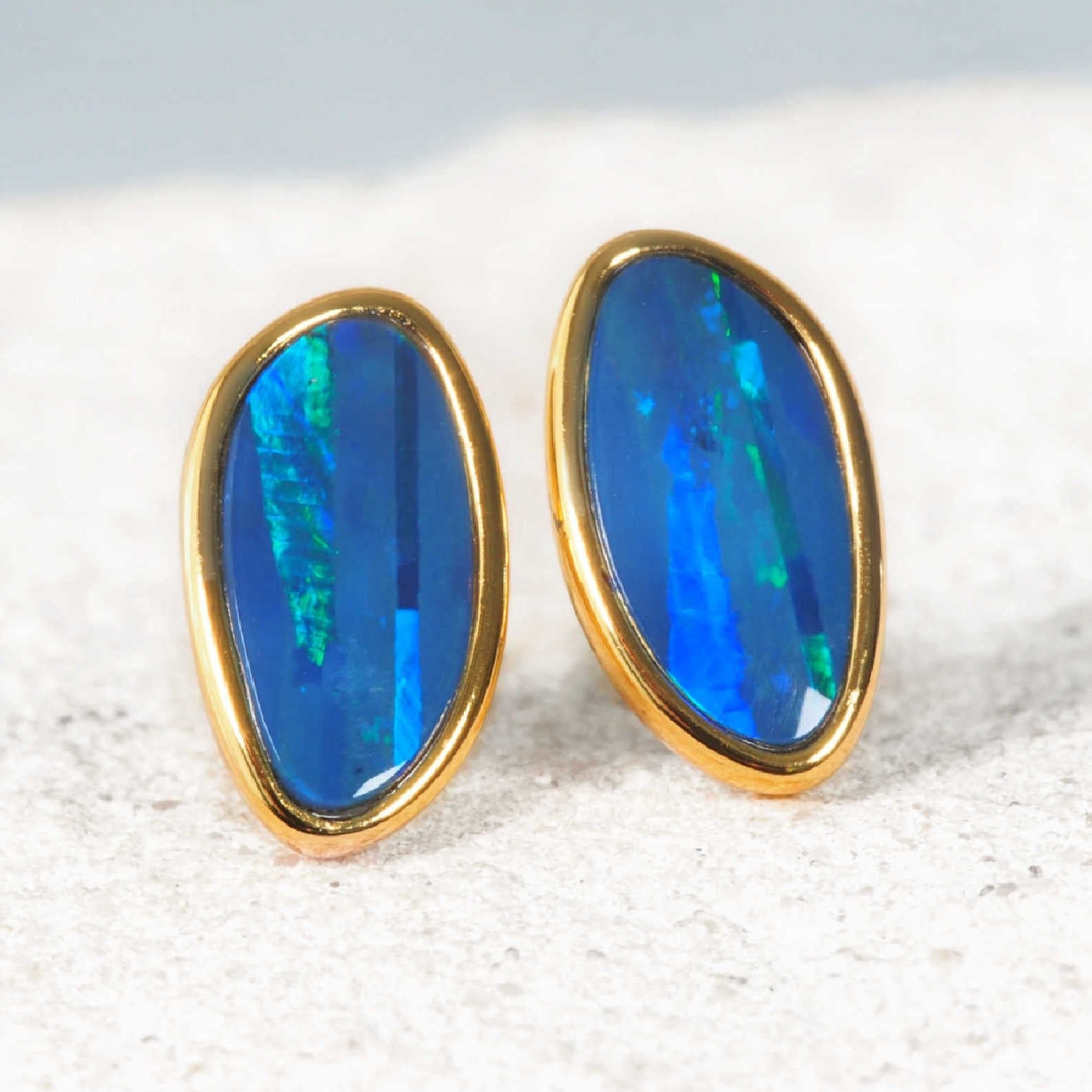 Pair of blue oval gemstone earrings with gold frames on a light background