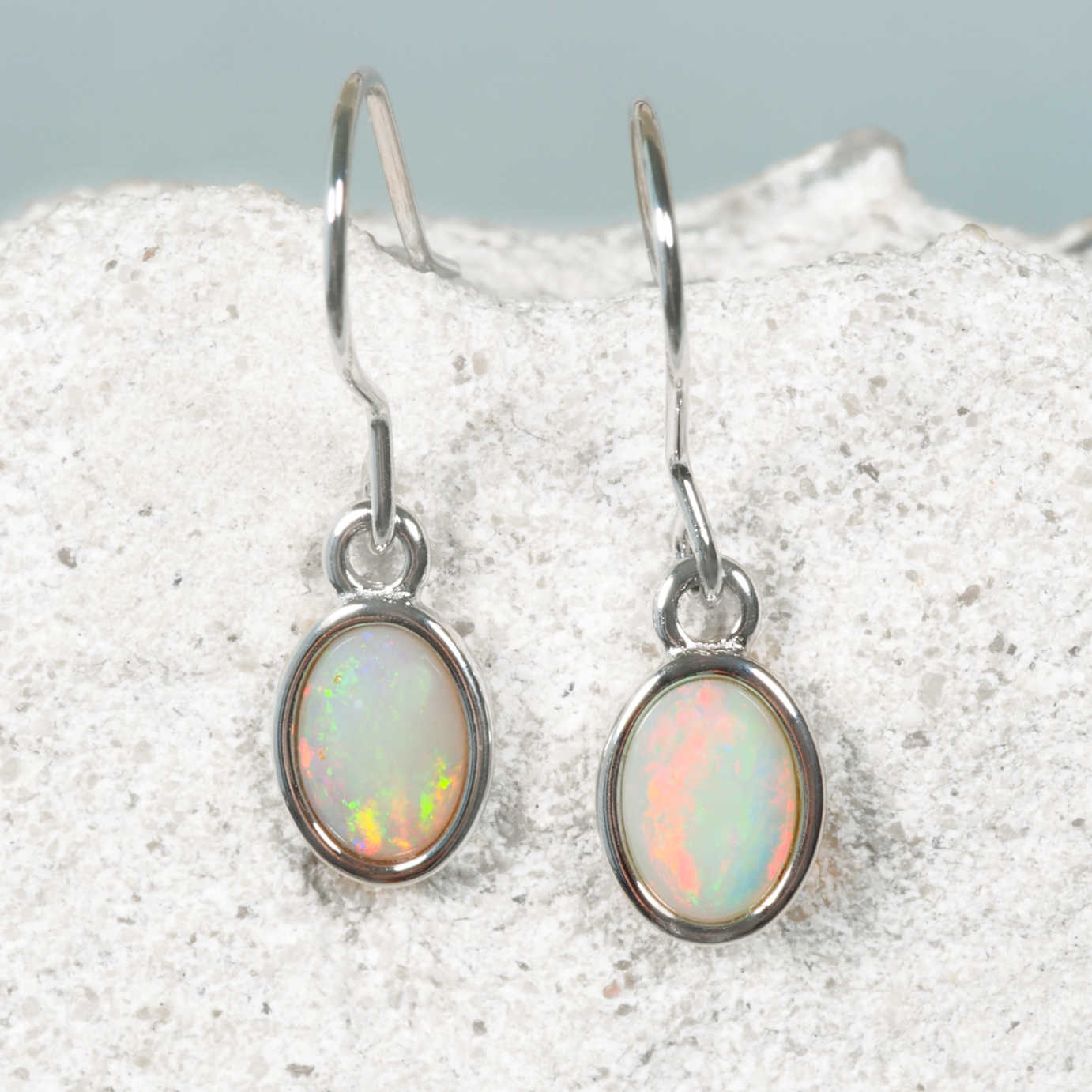 Opal earrings on a textured surface with a light background