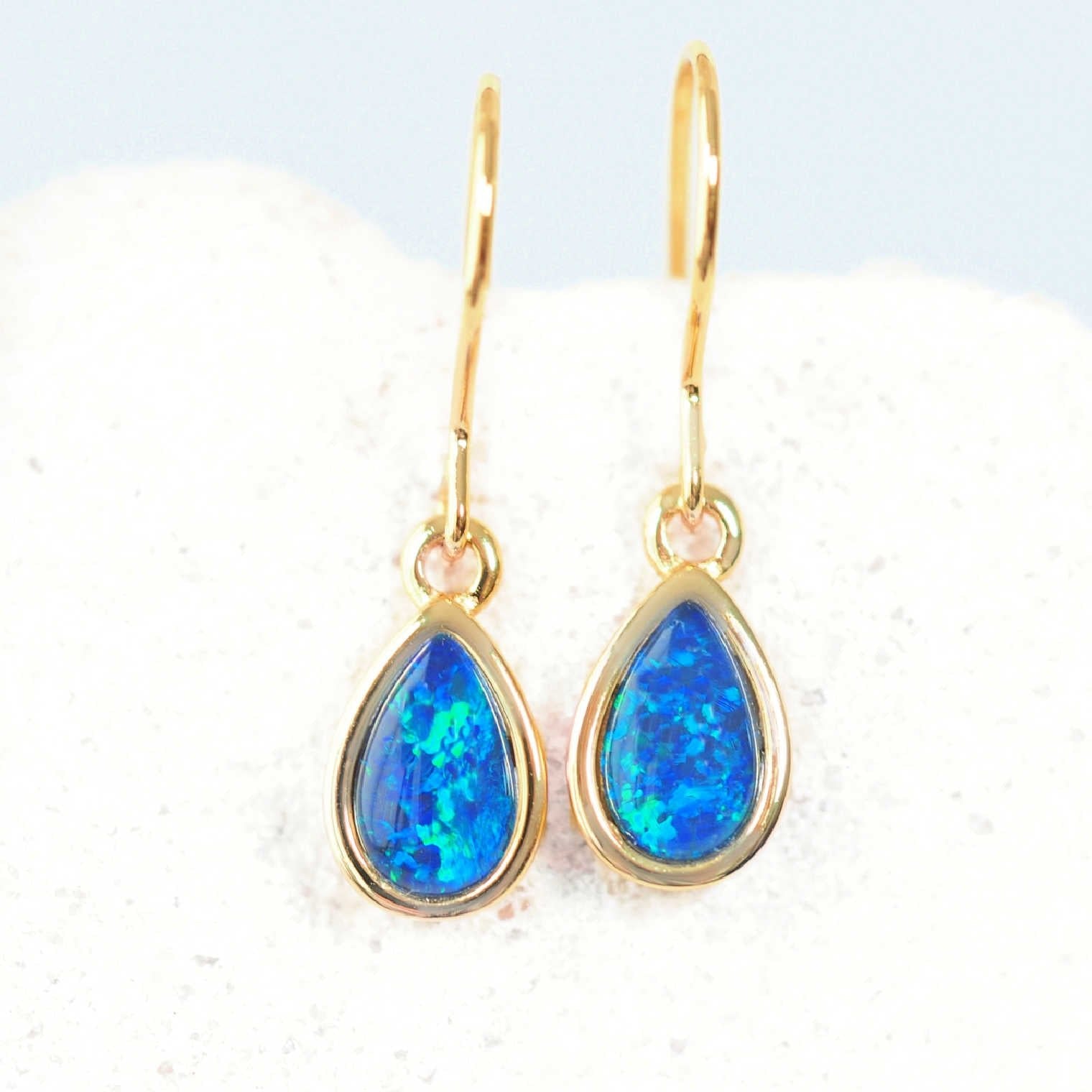 Gold earrings with blue teardrop-shaped gemstones on a white background