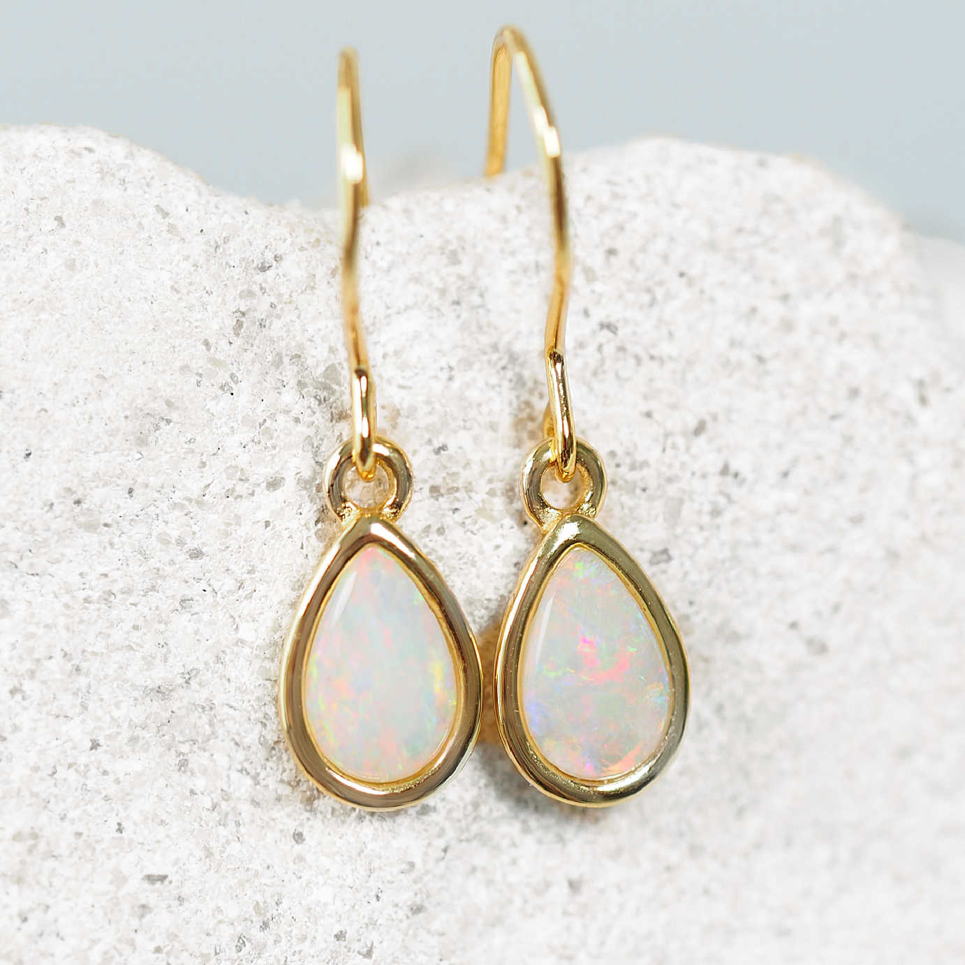 Gold opal earrings with teardrop-shaped gemstones on a textured surface