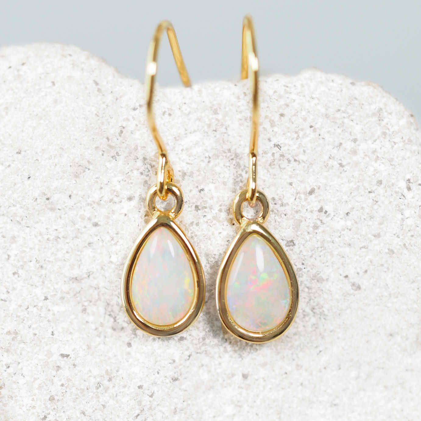 Gold teardrop earrings with opal stones on a textured white surface