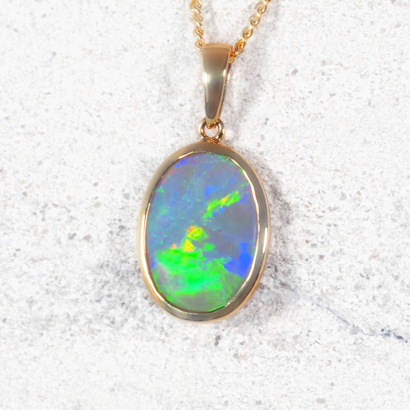 Lightning Ridge black opal pendant on a gold chain against a textured white background