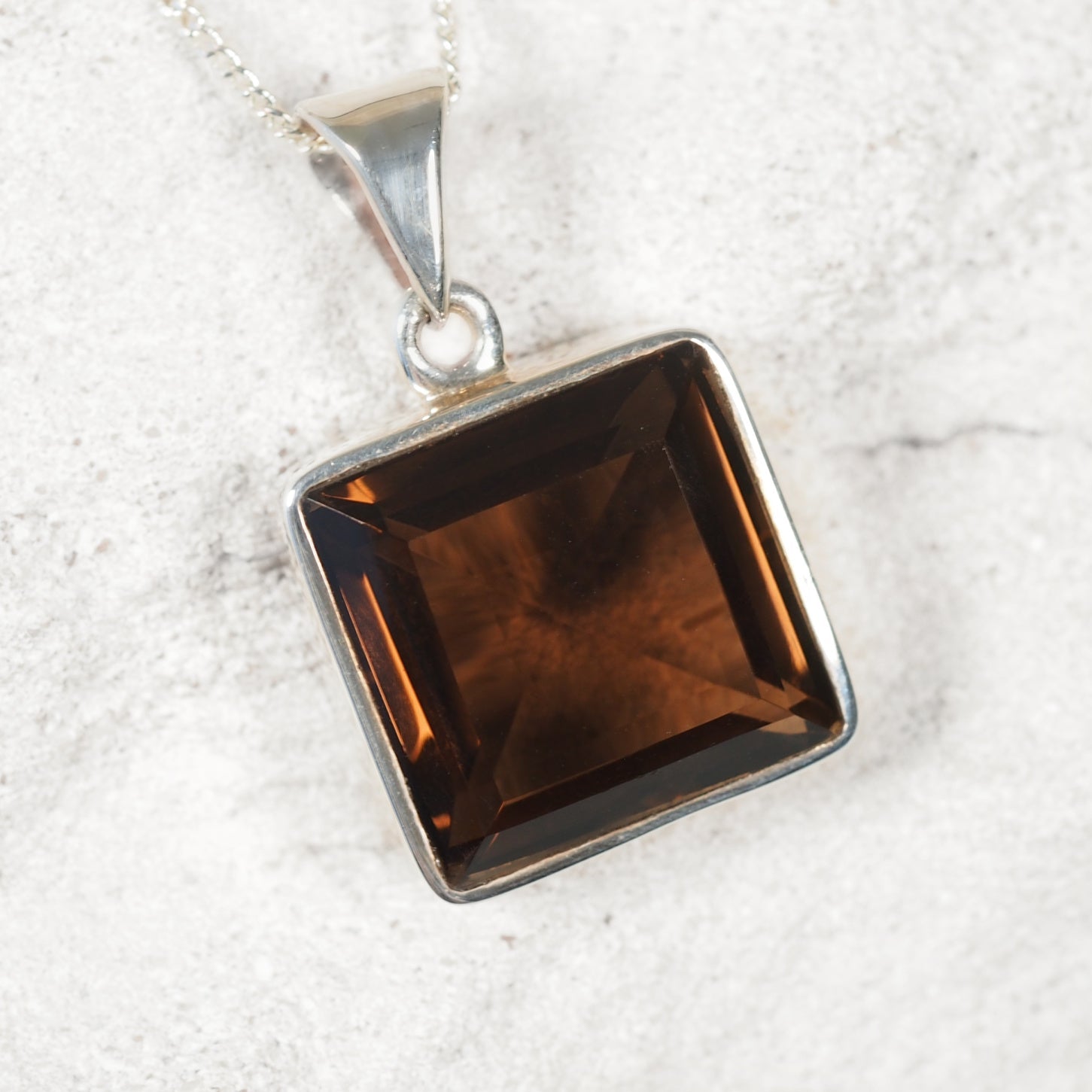 Square-shaped smoky quartz pendant on a silver chain against a white background