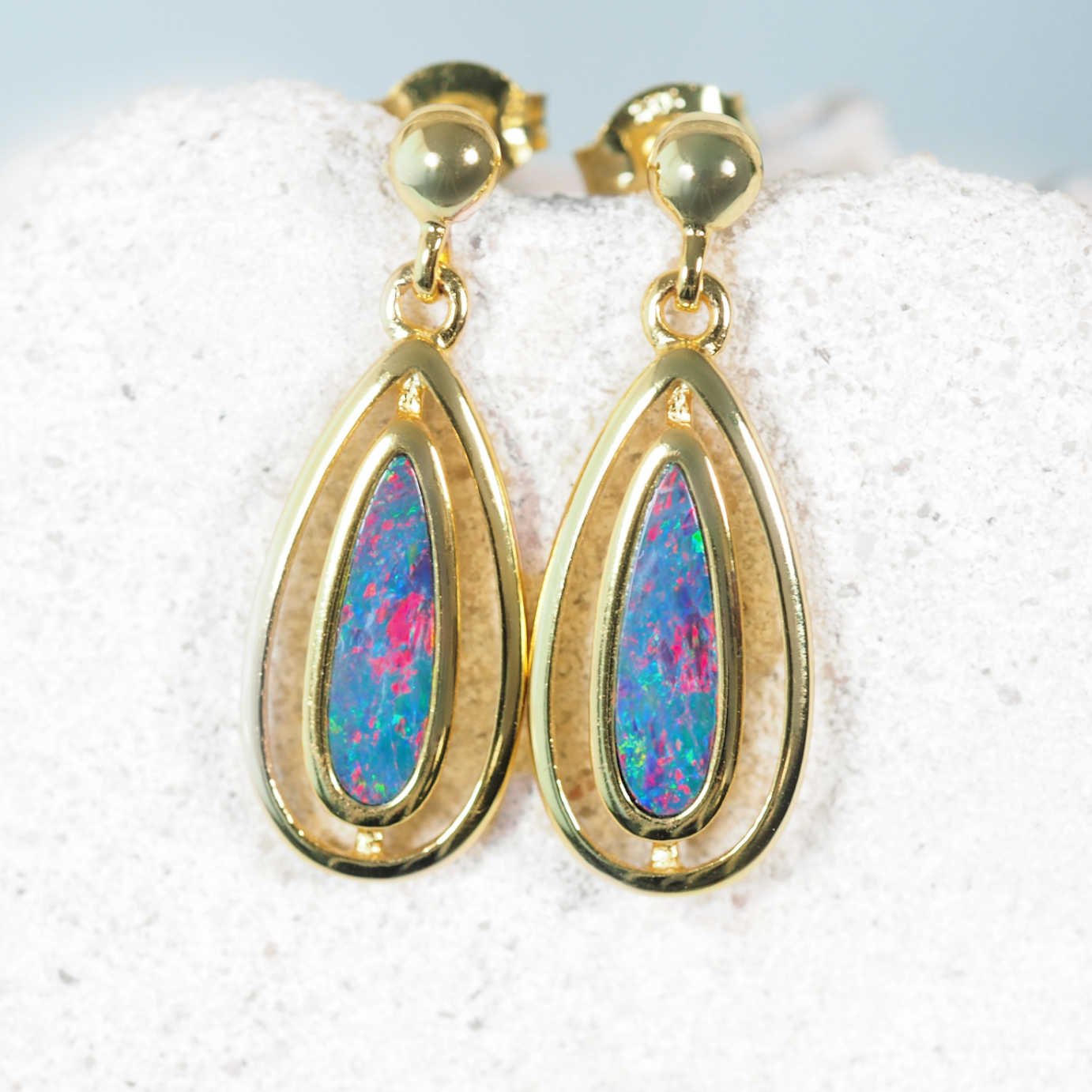 Gold earrings with colorful opal gemstones on a textured white surface