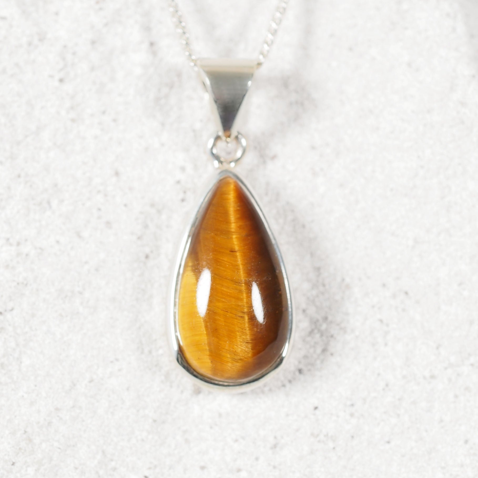 Teardrop-shaped tiger's eye pendant on a silver chain against a white background