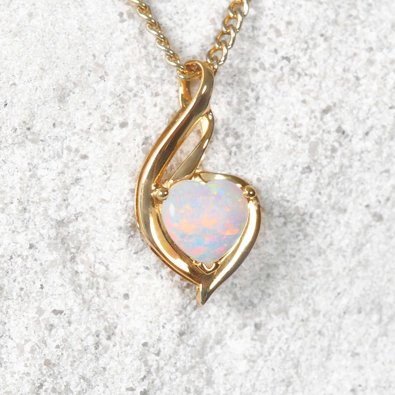 Gold necklace with a heart-shaped opal pendant on a textured white background