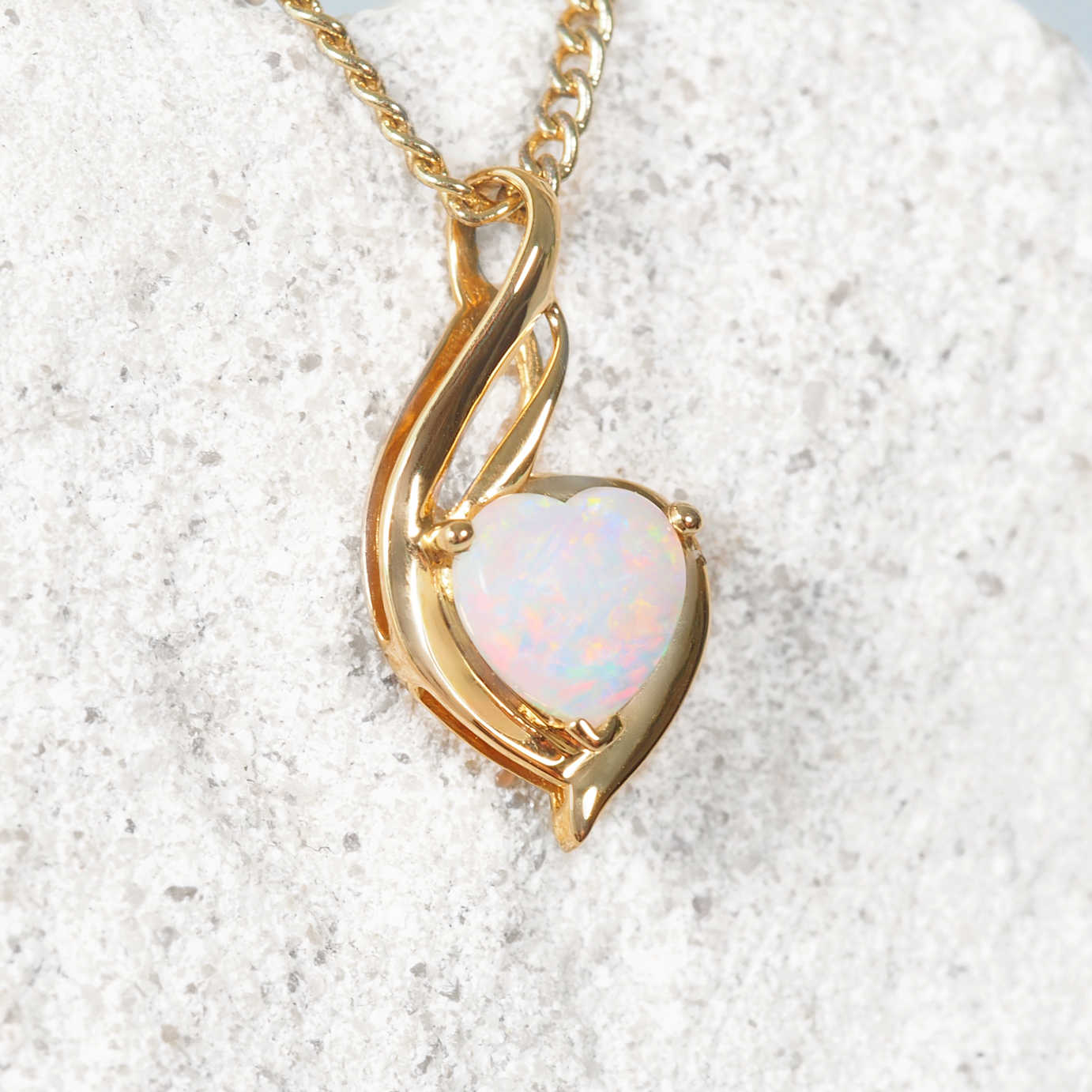 Australian gold necklace with a heart-shaped white opal pendant on a white rock background
