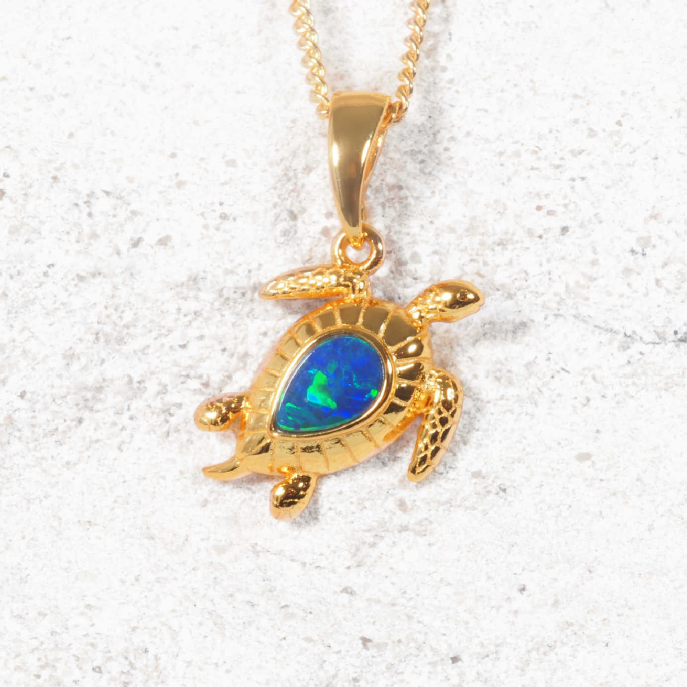 Gold turtle pendant with blue opal stone on a white sandy background