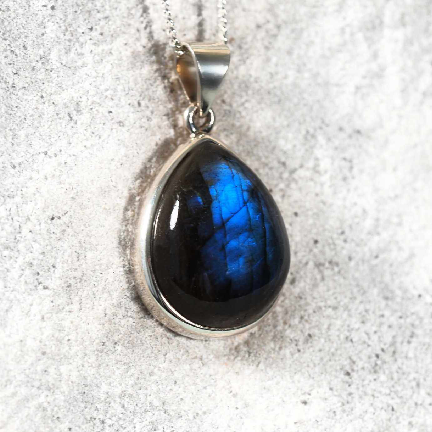 Dark Labradorite cabochon pendant in a sleek silver teardrop frame, glowing with delicate blue flashes