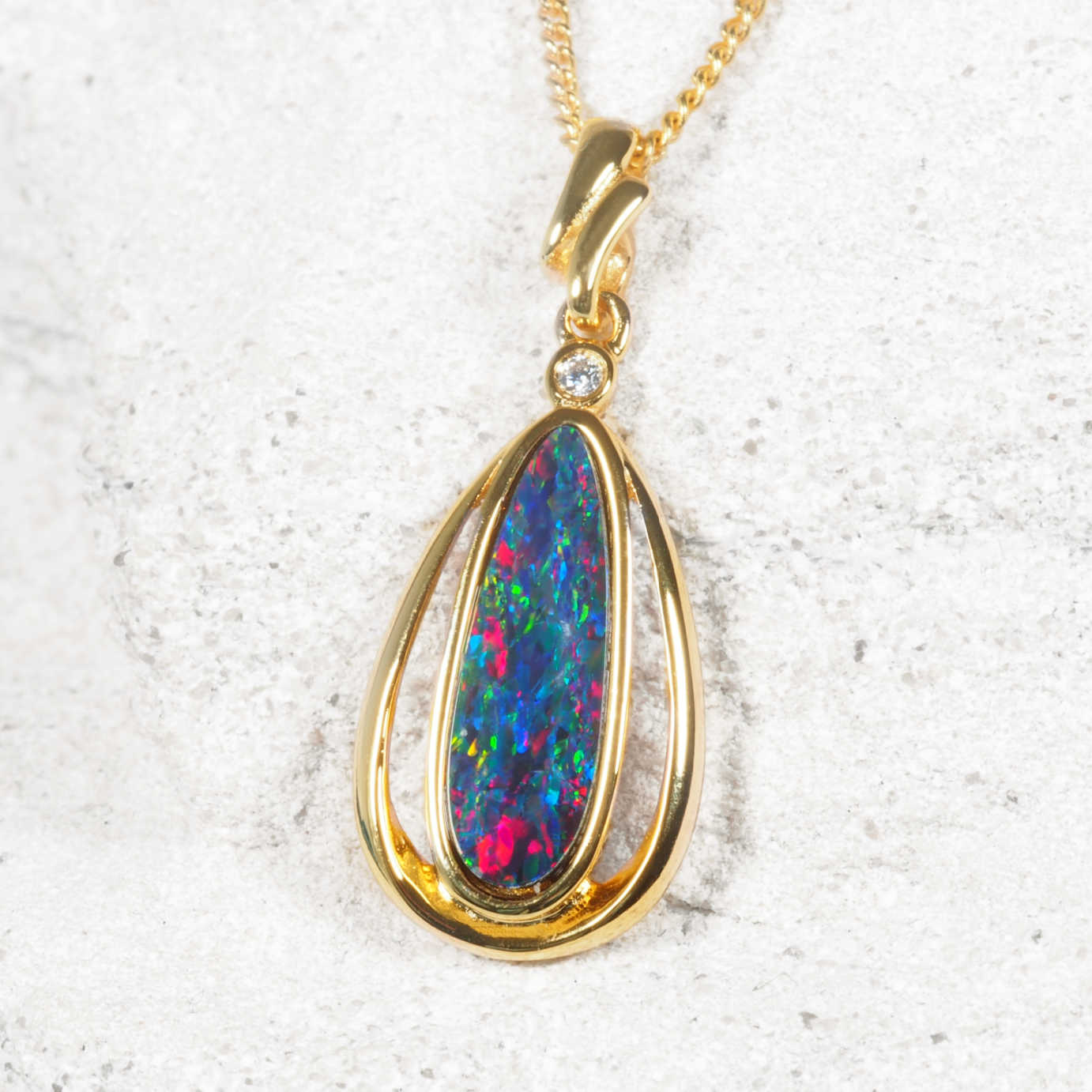 Gold pendant with a colorful opal gemstone on a textured white background