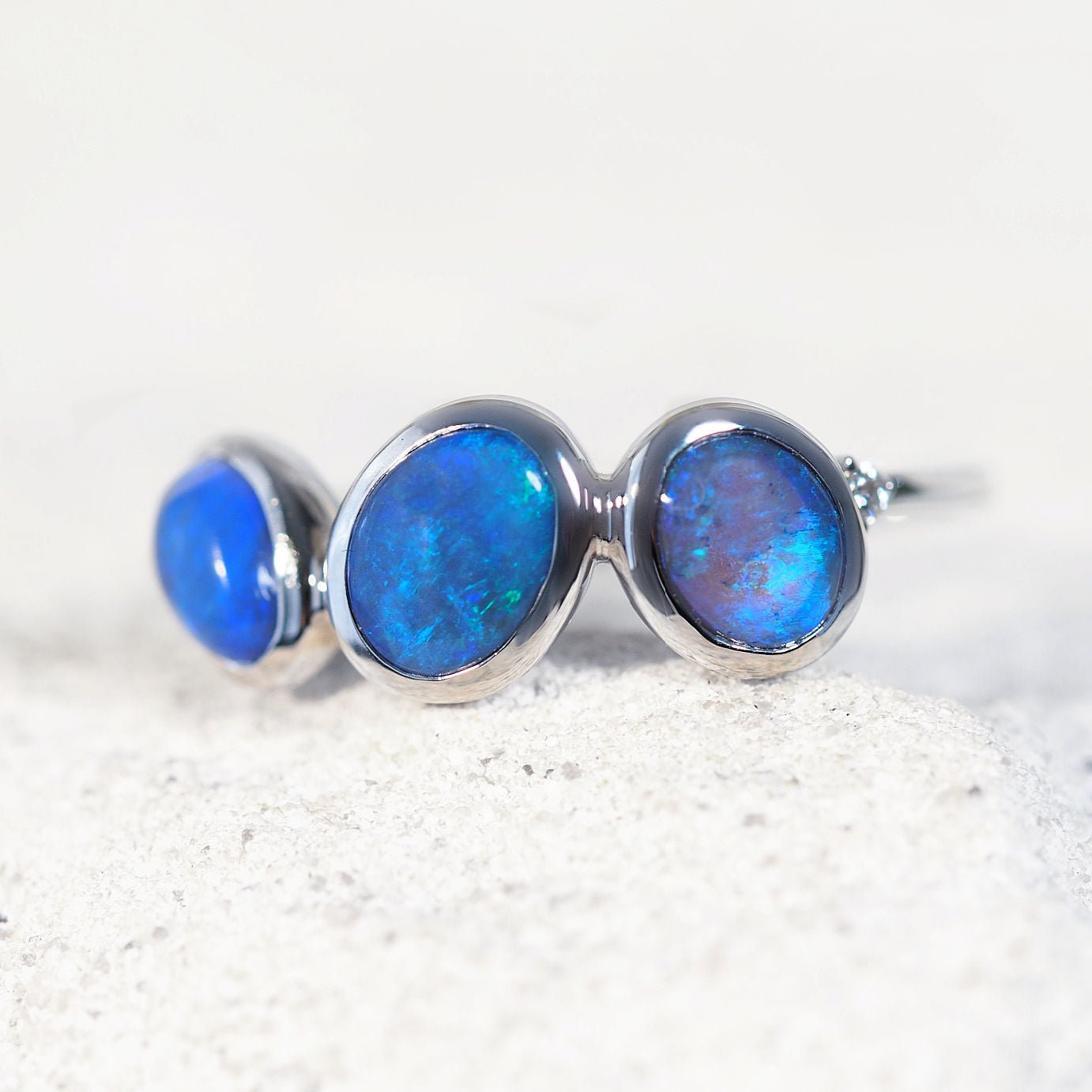 Three-stone opal ring with blue opal gemstones on a white background