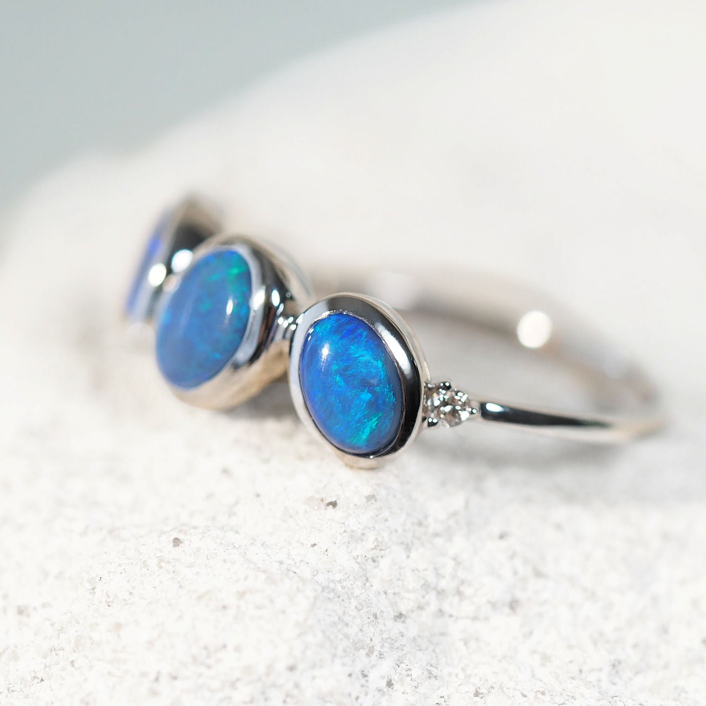 White gold opal ring with blue opal gemstones and diamonds on a light gray background